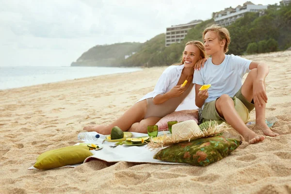 Саммер. Семейный пикник на пляже. Портрет молодой женщины с сыном, наслаждающейся обедом в тропическом океане. Мать и красавчик на отдыхе у моря. Органические фрукты и натуральные витамины. — стоковое фото