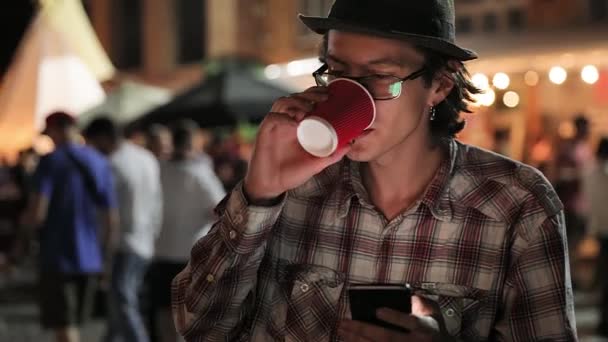 Junger Mann trinkt Kaffee und telefoniert abends auf der Straße — Stockvideo