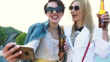 Dışarıda telefonda fotoğraf çeken, bira içen ve selfie çeken mutlu kadınlar.