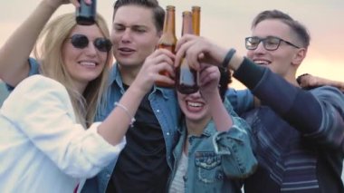 Mutlu arkadaşlar bira içiyor, şişelerle tezahürat yapıyor ve dans ediyor.