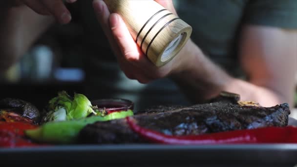 Essen in Großaufnahme. Mann würzt Steakfleisch mit gemahlenem Pfeffer — Stockvideo