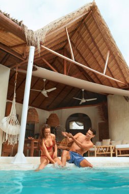 Havuzda Yaz Tatili. Moda Çifti Tropikal Villa 'da eğleniyor. Genç adam ve kadın su sıçratıyorlar ve gülüyorlar. Pozitif Duygular İçin Balayı Konaklama Merkezinde.
