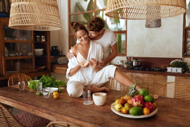 Sağlıklı beslenme. Tropikal Villa 'daki mutfakta öğle yemeği için taze organik yemek pişiren çift. Erkek, Tahta Masada Oturan Kadına Kucaklıyor. Yaz Tatilinde Doğal Vitaminler ya da Romantik Hafta Sonu.