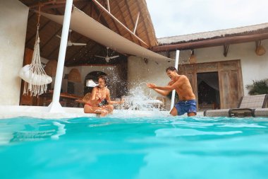 Yaz. Bir çift tatilde havuzda eğleniyor. Mutlu Adam ve Kadın Turkuaz Su Sıçratıyorlar ve Gülüyorlar. Tropikal tatil köyünde güzel bir kadın ve yakışıklı bir adam..