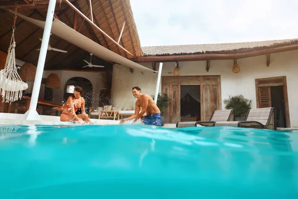 Nyár. Szerelmes pár a medencében Türkiz vizet fröcskölve és nevetve. Boldog férfi és nő szórakozik a trópusi villában. Divat férfi és nő Élvezi a nászutat Resort. — Stock Fotó