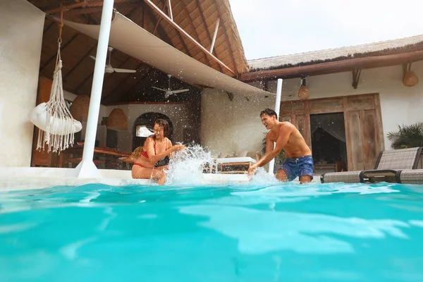 Egy pár a medencénél. Boldog férfi és nő szórakoznak a nyári vakáción vagy nászúton a trópusi villában. Divatférfi és női fröccsenő víz. Nyáron Luxury Resort A pozitív érzelmek. — Stock Fotó