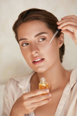 Güzellik Surat. Kadın yüz derisine gerekli yağı sürüyor ve başka yere bakıyor. Doğal E vitamini, Serum Kolajeni ve Hyaluronik Asitle Güzel Model Nemlendirici Derma.