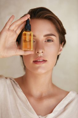 Cilt bakımı. Şişeyi Düşüren Yüzlü Kadın 'ın Güzel Portresi. Doğal Kozmetik Ürünleri Sıvı, Parlak ve Sağlıklı Yüz Derisi İçin Model Kullanımı. Yaşlanma Karşıtı Terapi İçin Temel Yağ.