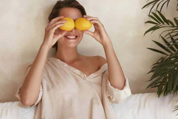 レモンを楽しんでいる女性。顔の近くにジューシーな柑橘類を保持し、自然の化粧でモデルの美しさの肖像画.有機ビタミンC｜滑らかで放射性で光るダーマのための. — ストック写真