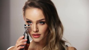 Kirpik Aracı. Makyajlı kadın elinde bigudi tutuyor.