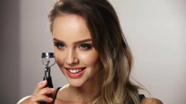 Kirpik Aracı. Makyajlı kadın elinde bigudi tutuyor.