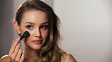 Güzel yüzlü bir kadın, fırçayla allık sürüyor.