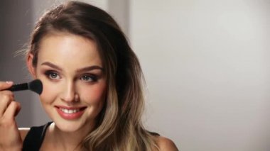 Güzel yüzlü bir kadın, fırçayla allık sürüyor.