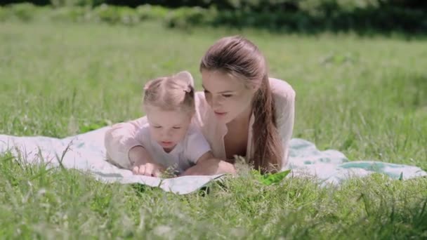 幼い母と娘読書本は公園で草の上に横たわる — ストック動画
