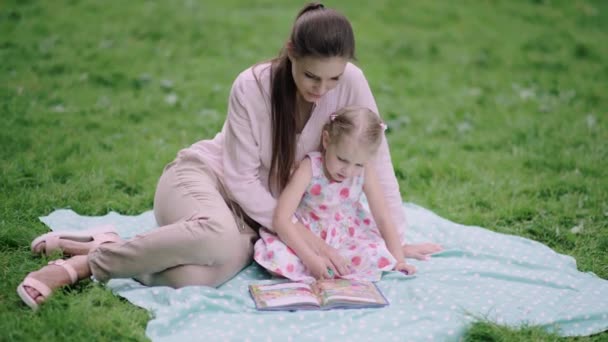 幼い母と娘読書本は公園で草の上に横たわる — ストック動画