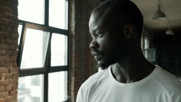 Retrato del hombre negro mirando a la cámara de pie cerca de las ventanas — Vídeo de stock