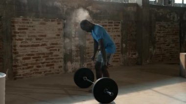 Spor adamı ellerinde tebeşir tozu ve spor salonunda ağırlık kaldırıyor.