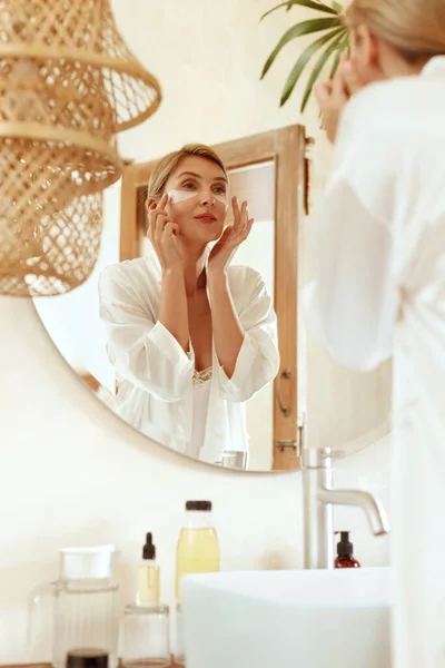 Rotina de cuidados com a pele. Mulher com manchas sob os olhos em pé no banheiro e olhando para o espelho. Lady In Fashion Silk Pajama Usando Hidrogel Com Ácido Hialurônico E Colágeno Para Procedimento De Beleza Em Casa. — Fotografia de Stock