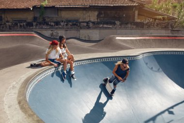 Yaz. Paten parkında kaykay yapan kaykaycı arkadaşlar. Dışarıdaki sıradan giyinmiş bir grup insan. Beton Rampada Oturan Hippi Kızlar, Kaykay Yapan Adam. Kentsel Yaşam Tarzı Olarak Ekstrem Spor.