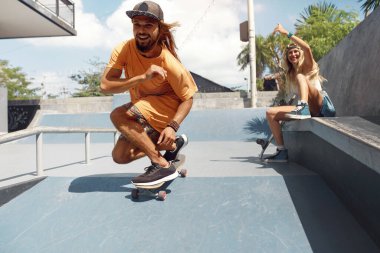 Yaz. Kaykaycı Arkadaşlar Kaykay Pisti 'nde. Erkek ve kız günlük kıyafetleriyle dışarıda eğleniyorlar. Beton rampadan kaykaylı mutlu çift eğitimi. Kentsel Yaşam Tarzı Olarak Ekstrem Spor.