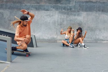 Yaz. Kaykaycı Arkadaşlar Kaykay Pisti 'nde. Erkek ve kızlar günlük kıyafetleriyle dışarıda eğleniyorlar. Mutlu insanlar Beton Rampada kaykayla antrenman yapıyor. Kentsel Yaşam Tarzı Olarak Ekstrem Spor.