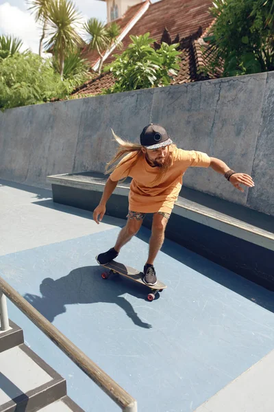 Subcultura. Homem patinador no Skatepark. Guy em roupa casual com equipamento desportivo moderno montando no skate na rampa de concreto. Atividade extrema como estilo de vida urbano. — Fotografia de Stock