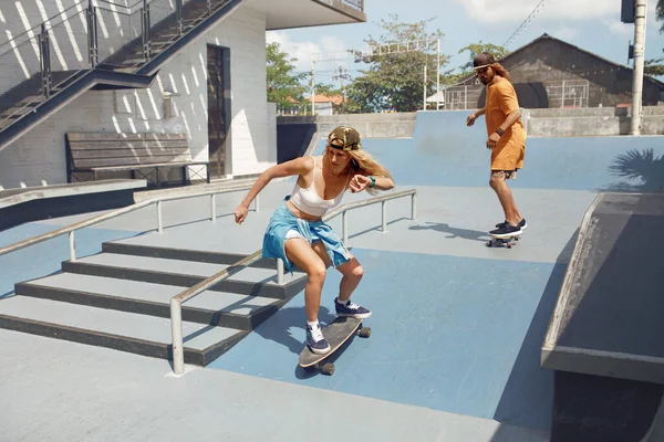 Skateboarding. Passeios de casal em skates no Skatepark. Patinadores em roupas casuais fazendo truques na rampa de concreto. Atividade de verão como estilo de vida. Esporte extremo para homens e meninas urbanos ativos. — Fotografia de Stock