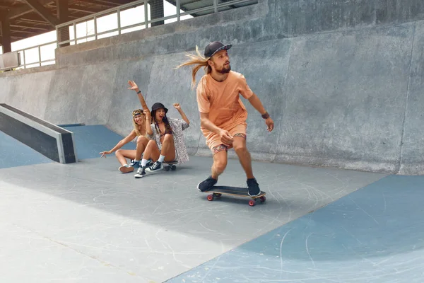 Skateboarding. Homem cavalgando no skate no Skatepark. Grupo de patinadores em roupa casual fazendo truques na rampa de concreto. Atividade de verão como estilo de vida. Esporte extremo para homens e meninas urbanos ativos. — Fotografia de Stock