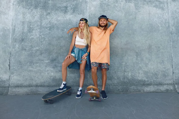 Kaykay portresi olan çift. Adam ve kız, kaykay parkında beton duvara karşı gelişigüzel giyinmişler. Kentsel Alt Kültür ve Kaykay Şehirdeki Aktif İnsanların Yaşam Tarzı.