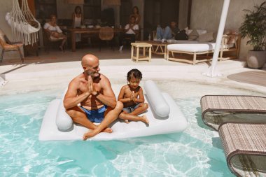 Havuz. Oğlu babası şişme su yatağında meditasyon yapıyor ve yüzüyor. Baba ve Çocuk, Tropikal Tatil Köyü 'nde tatilin tadını çıkarıyorlar. Villa 'da Aile Hafta Sonu. Yaşam Tarzı Olarak Mutluluk.