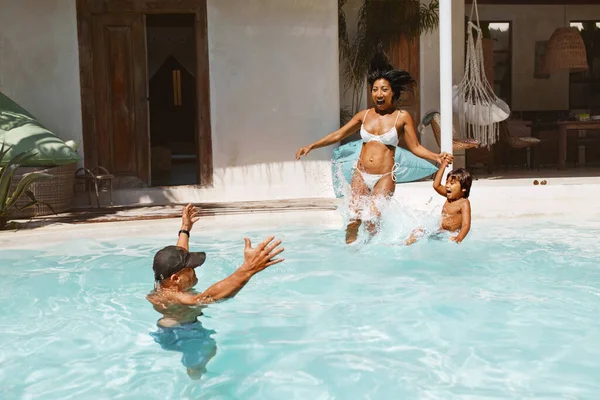 Diversión familiar en la piscina. Madre e hijo saltando en el agua con salpicaduras. Padres y niños disfrutando del ocio en fin de semana. Actividad de verano en Tropical Resort para la felicidad. — Foto de Stock
