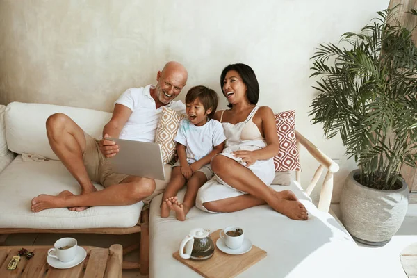 Keluarga bahagia di Sofa. Portrait of Mixed Race Parents With Little Son Using Tablet And Enjoying Leisure On Summer Vacation At Tropical Resort (dalam bahasa Inggris). Etnis yang berbeda Mom and Dad With Boy On Weekend. — Stok Foto