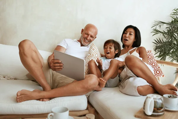 Семья использует планшет по выходным. Happy Interracial Parents with Little Boy Sitting On Sofa, Using Portable Digital Device and Having Fun At Home. Мама, папа и сын на летних каникулах в тропическом курорте. — стоковое фото