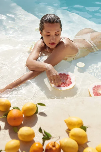 シトラスとプールで美しいモデルの肖像画。新鮮なエキゾチックなフルーツを楽しむビキニの女たち｜SPA. — ストック写真