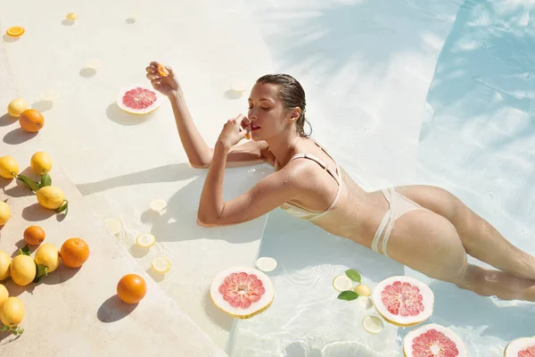 Femme dans la piscine. Agrumes pour une peau parfaite et un corps mince. Belle fille en bikini au spa tropical. — Photo