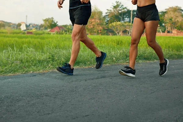 Couple courant sur la route au paysage tropical le matin. Homme et femme sur la séance d'entraînement de jogging près de champs de riz vert. — Photo