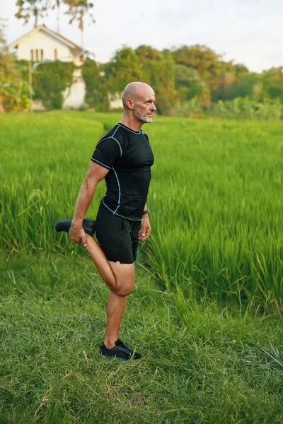 Caucásico Hombre estiramiento antes de correr entrenamiento al aire libre. Hombre deportivo calentándose antes de correr en el campo de arroz. —  Fotos de Stock