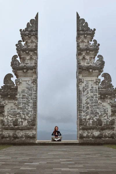 Hermosa chica en loto Pose meditando cerca de las puertas del cielo en el templo de Pura Lempuyang en Bali, Indonesia. Mujer joven tranquila y pacífica sentada con las piernas cruzadas cerca de la arquitectura antigua, Asia. — Foto de Stock