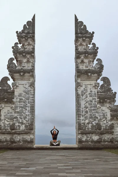 Hermosa chica en posición de loto meditando en el templo de Pura Lempuyang en Bali, Indonesia. Mujer joven y pacífica sentada con las piernas cruzadas y las manos sobre la cabeza, Puertas del cielo, Asia. — Foto de Stock