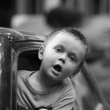 Kameraya bakarak araba pencereden dışarı eğilmiş küçük ifade çocuk bardak siyah ve beyaz. 