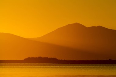 Gün batımında dağların ve gölün turuncu manzarası