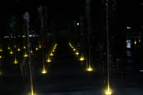 夜景中美丽多彩的浅水喷泉 黑色背景的喷泉上的彩色水型 — 图库照片