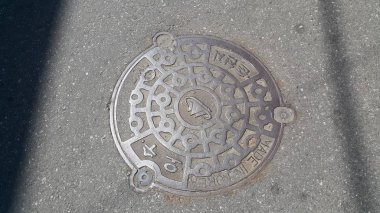 Asfalt yol altında drenaj veya kanalizasyon üzerinde bir rögar kapağı üst görünümü.