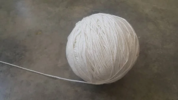 Белый шар из ниток тканой пряжи для вязания на сером фоне пола — стоковое фото