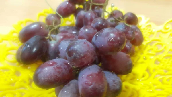 Vista ravvicinata di grappoli di uva bruna serviti in vaschetta di plastica gialla — Foto Stock