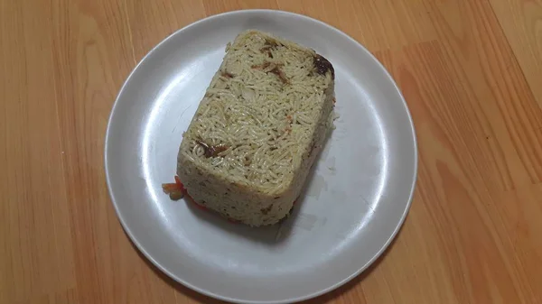 Крупный план замороженного белого рисового пирога в белой тарелке над деревянным полом — стоковое фото