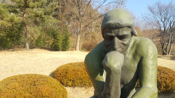 Düşünür Auguste Rodin'in yeşil heykeli, bir kayanın üzerinde çıplak ayarı — Stok fotoğraf