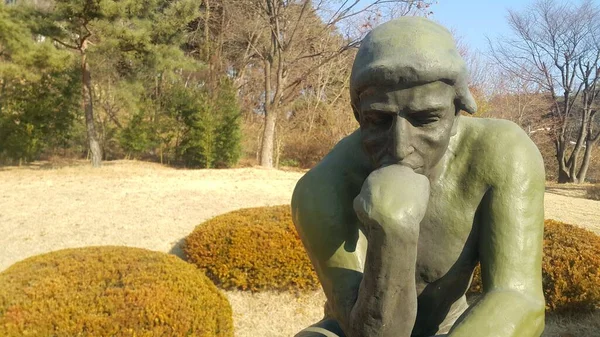 Green statue of thinker Auguste Rodin, setting naked on a rock — Stock Photo, Image