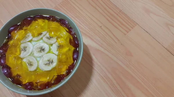 Cremige süße Pudding mit Bananenstücken auf Oberfläche inbowl auf Holzboden — Stockfoto