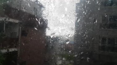 Metal bir gazlı bezin arkasında yağmurlu mevsim manzarası ve pencere camında yağmur damlaları